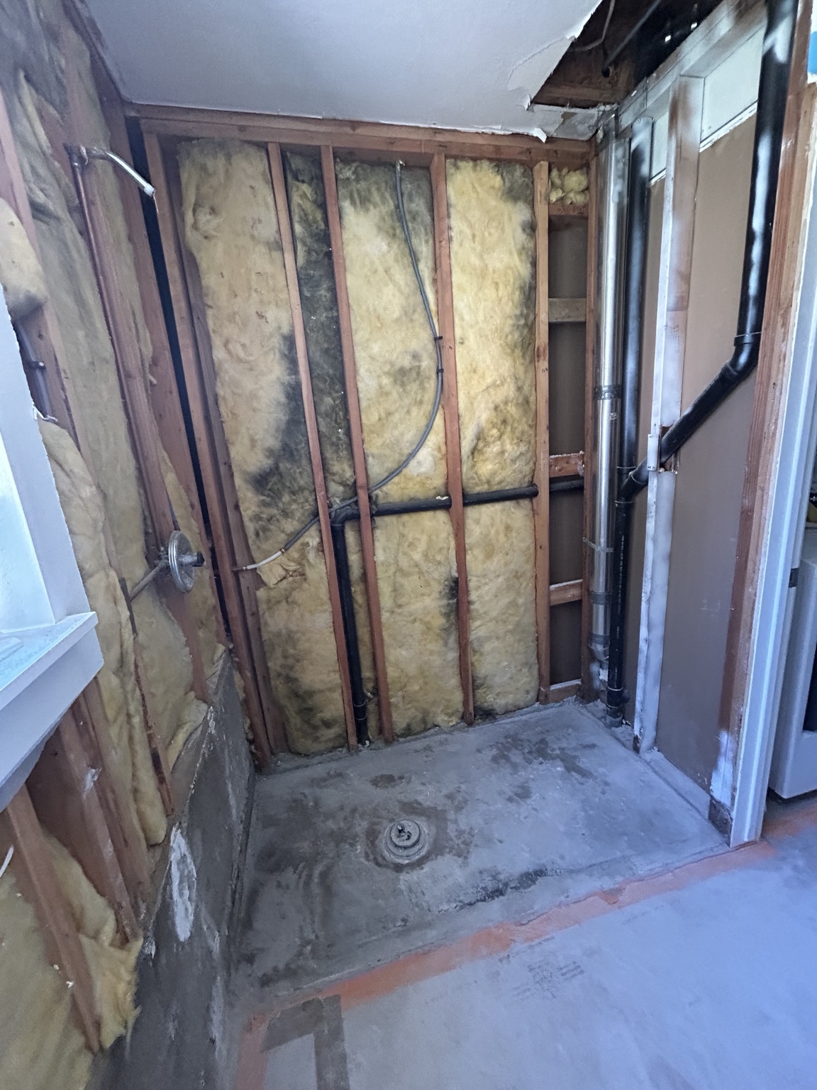 Shower after tile tear-out, showing exposed framing, plumbing and the shower base